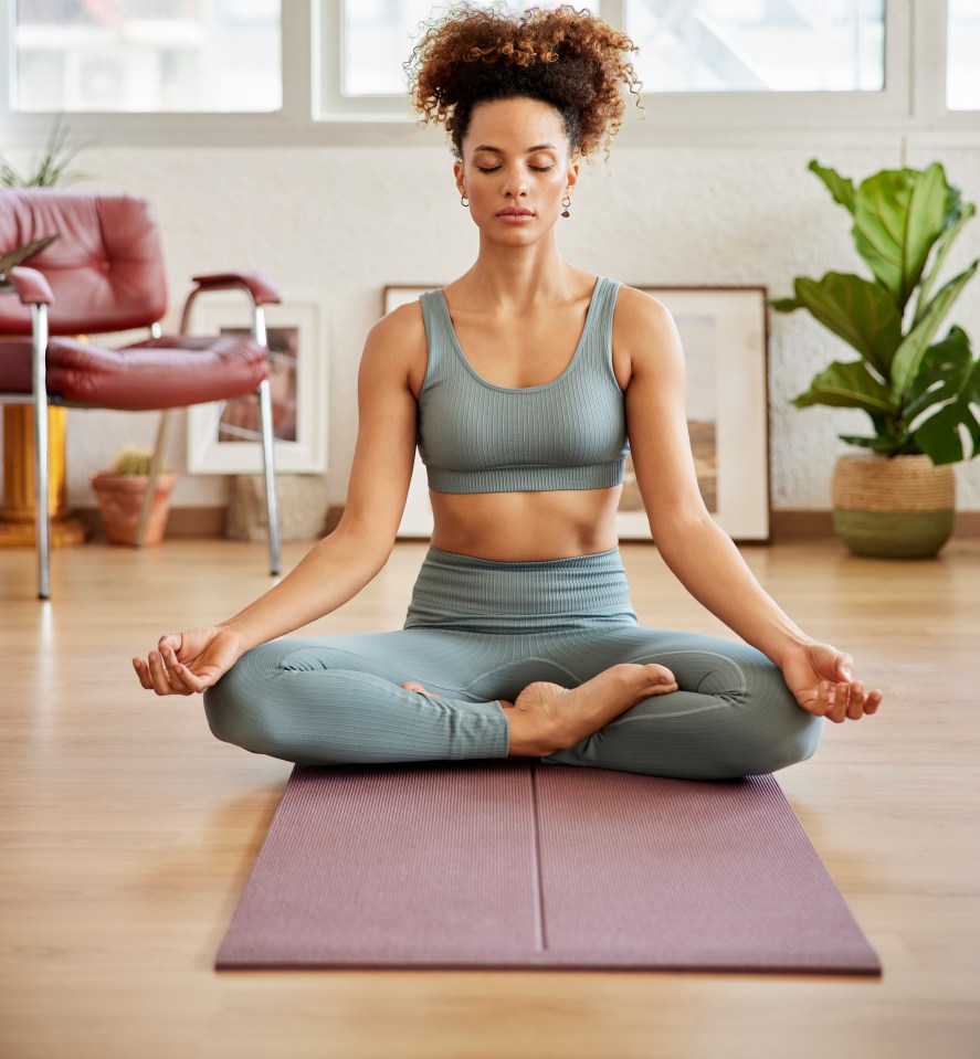 Young woman with curly hair meditating in lotus position on an exercise mat at home.