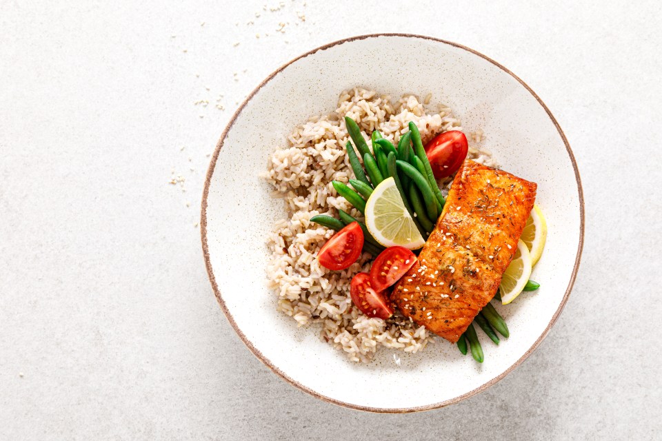 Baked salmon fillet with rice, green beans, tomatoes, and lemon slices.
