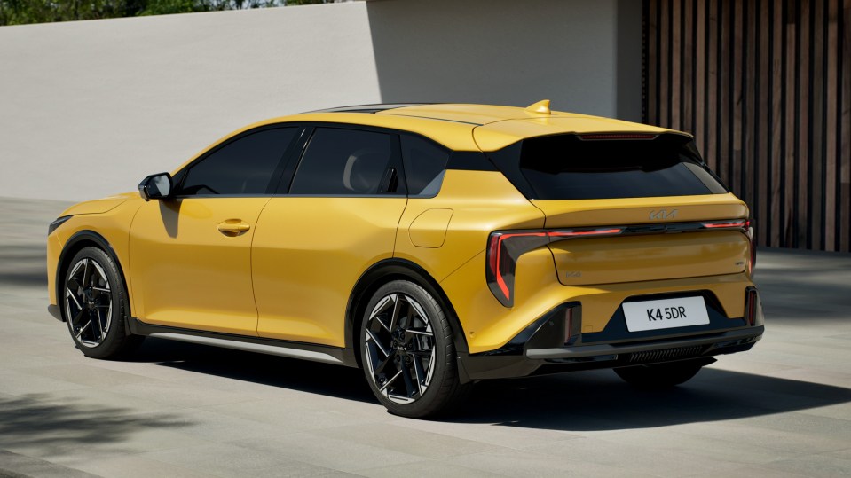 Rear view of a yellow Kia K4 5DR hatchback parked outside a modern building.