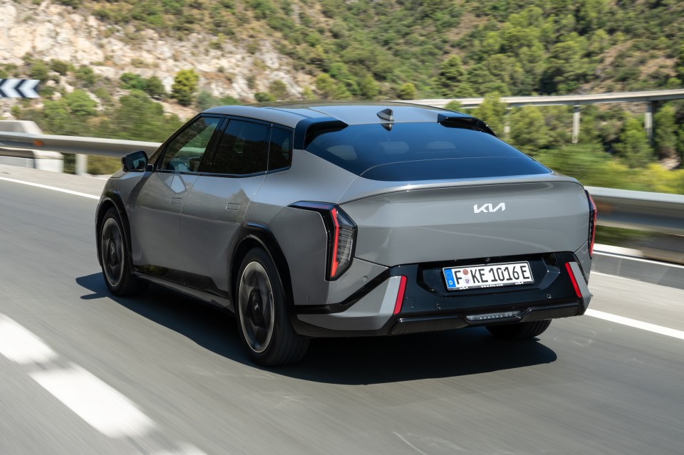 Rear view of a grey Kia EV6 driving on a highway, with mountains in the background.