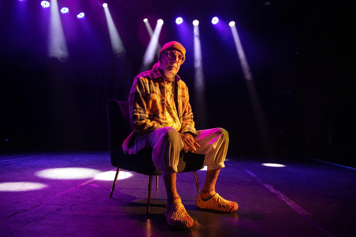 A man in shades sits below purple lights.