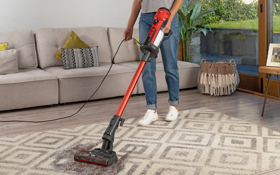 Woman vacuuming a rug with a red and black corded vacuum cleaner.