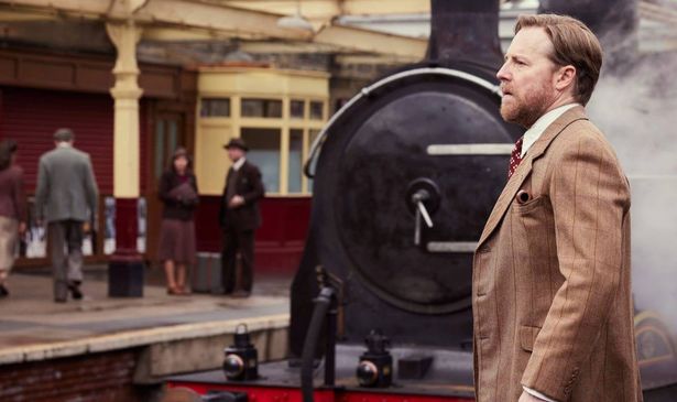 A man at a train station with a vintage train next to him