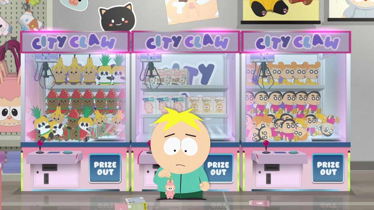 A boy in a green coat standing in front of a row claw machines filled with toys.