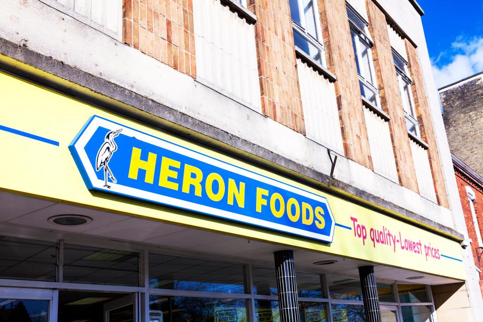 Heron Foods shop sign with a heron logo and "Top quality - Lowest prices" tagline.