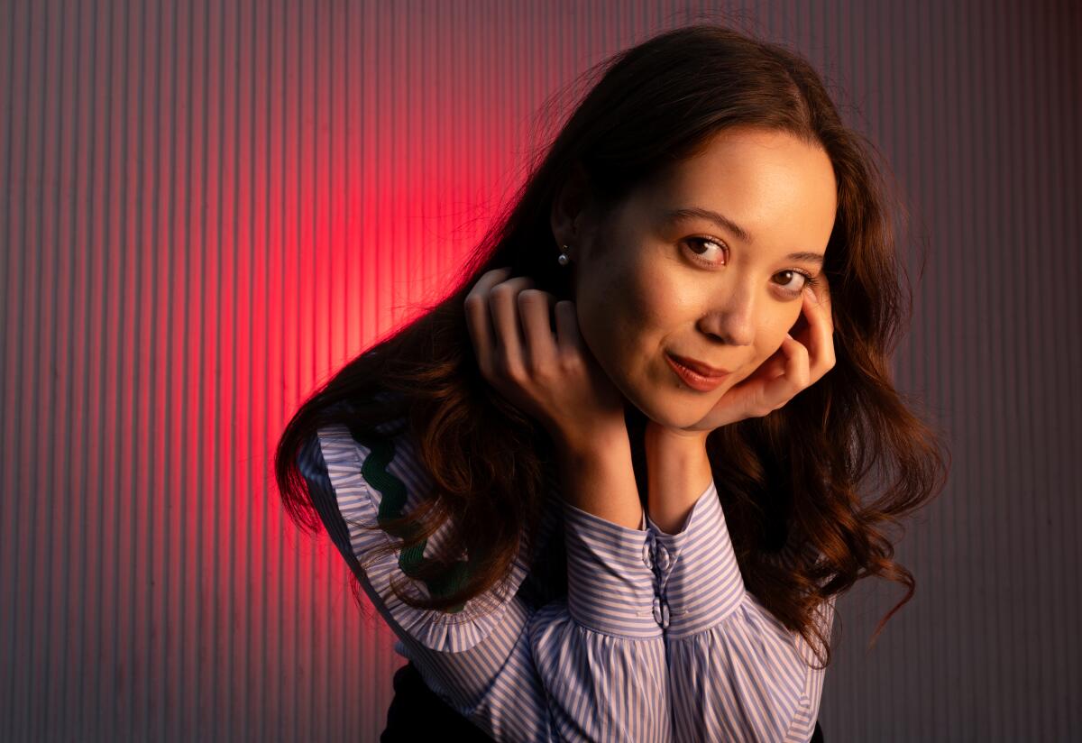 A woman with long brown hair smiling, holding her face in her hands
