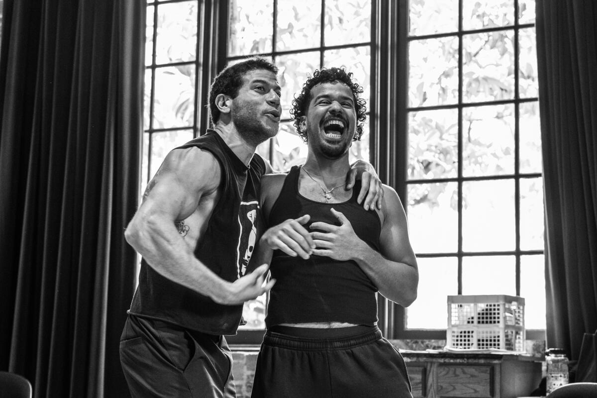 A black-and-white photo of two actors in tank tops rehearsing a play.