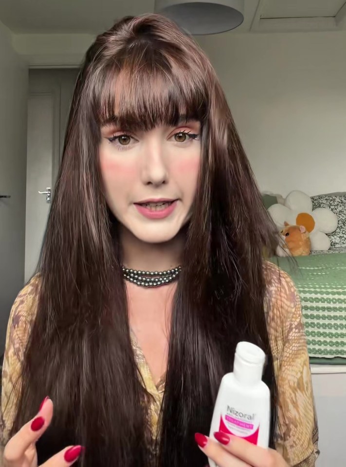A woman holds a bottle of Nizoral shampoo, showcasing it to the camera.