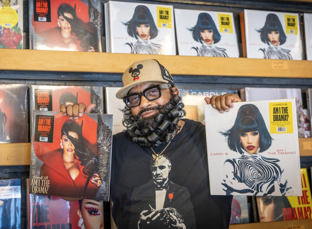 A bearded man holds Cardi B albums in a record store.