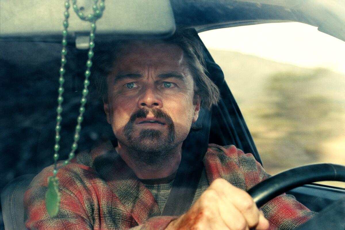 An alarmed, bearded man sits behind the wheel of a car.