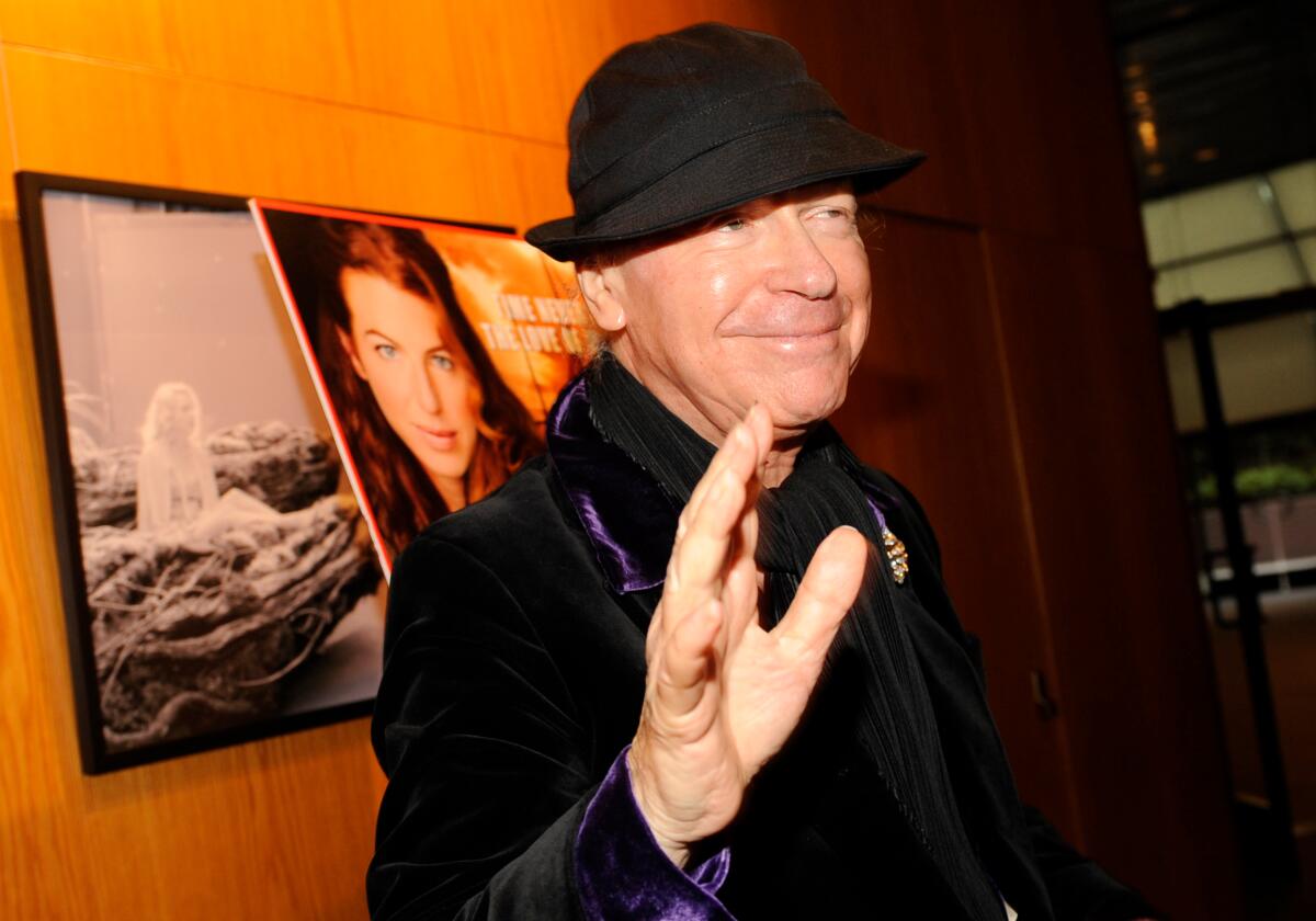 A man in a black hat waves to a photographer.