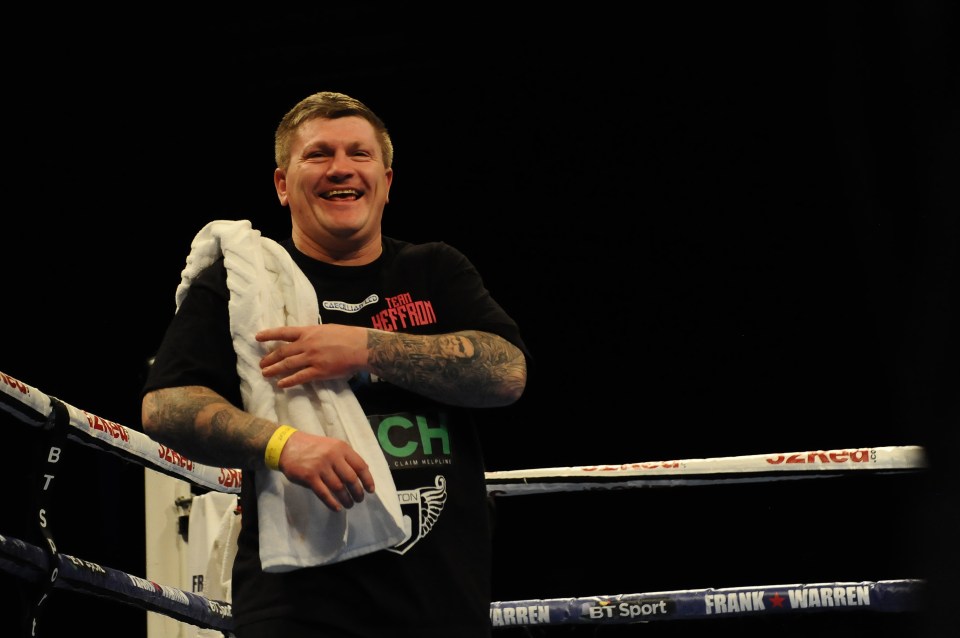 Ricky Hatton, wearing a black shirt and white towel, jubilantly laughs in a boxing ring.