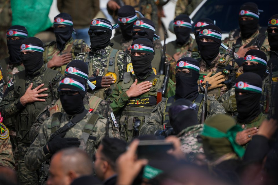 Hamas fighters in formation, wearing military fatigues and black balaclavas with Palestinian flag headbands.