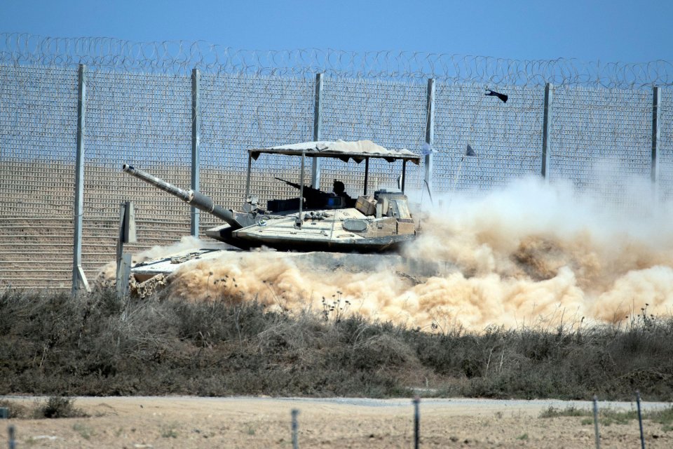 An Israeli IDF tank on the move along the border fence with the northern Gaza Strip, kicking up a large cloud of dust.