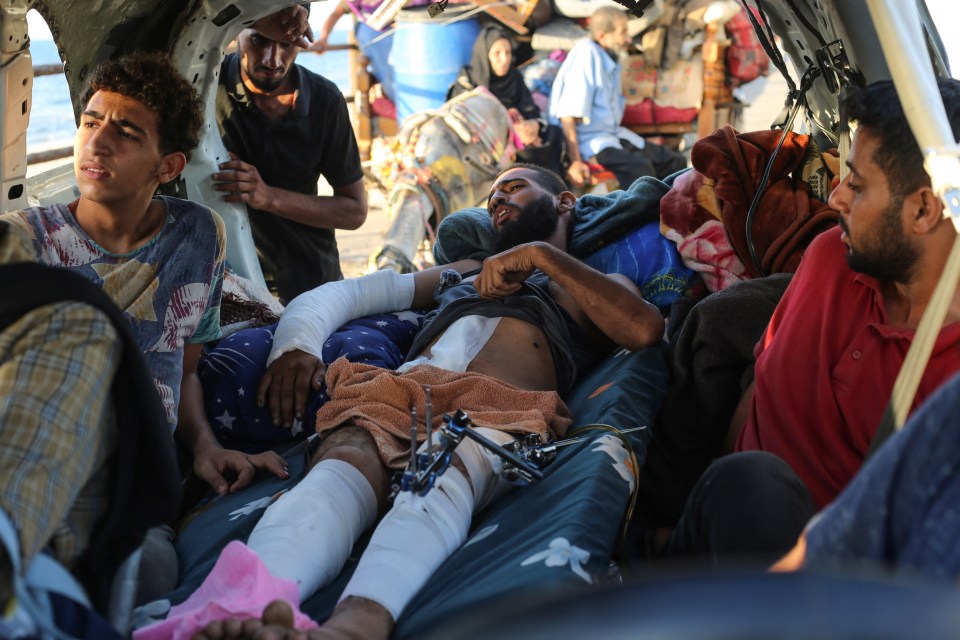 A wounded man lies in a vehicle with other displaced Palestinians, with the sea visible in the background.