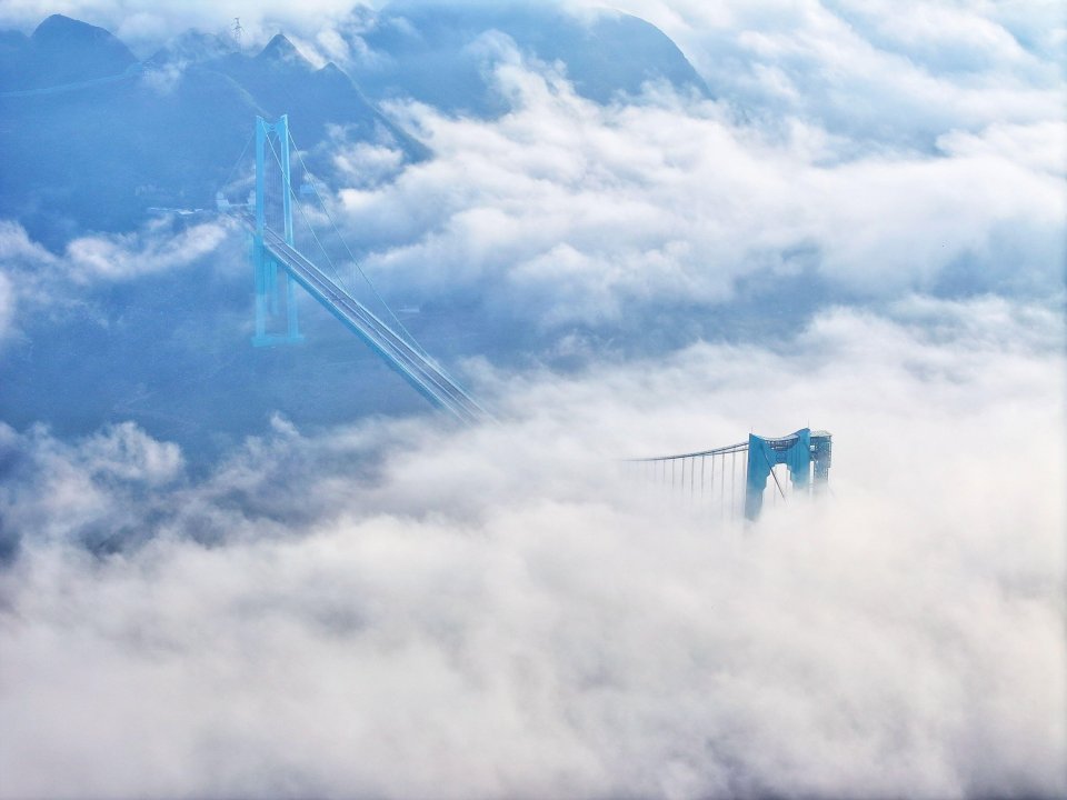 An aerial view of the Huajiang Grand Canyon Bridge partially obscured by clouds.