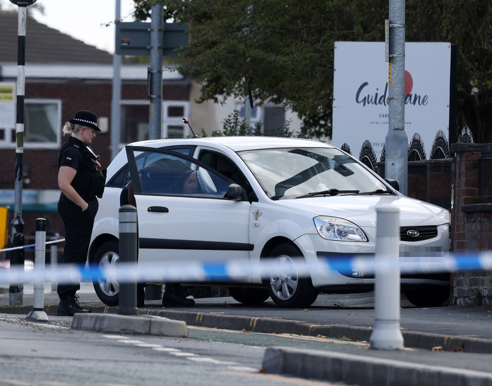 Police officer standing next to a white car with an open door on Guide Lane.