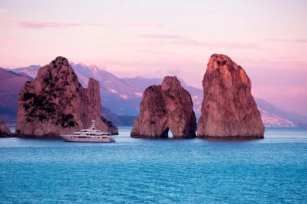 Luxury yacht is anchored near Faraglioni Rocks at sunset, Isola di Capri, Campania, Italy.