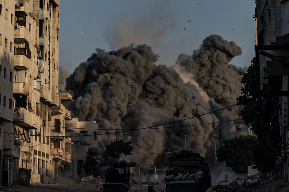 Smoke billows from the bombed Mekka Tower, surrounded by damaged buildings.