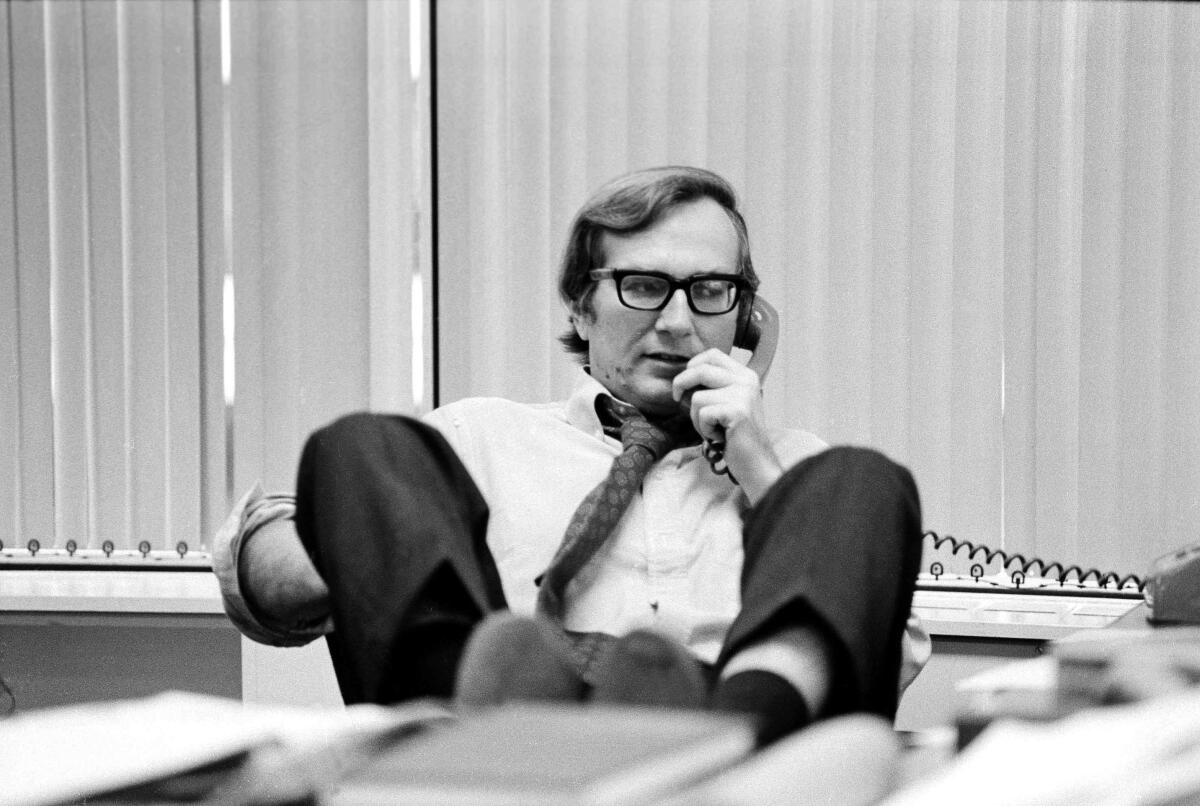 A man with his feet on his desk speaks on the phone.