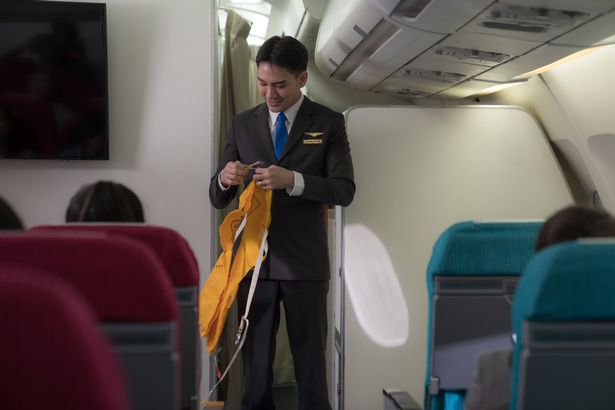 Cabin Crew or Steward staff airline demonstrate safety procedures to passengers prior to flight take off in cabin airplane.