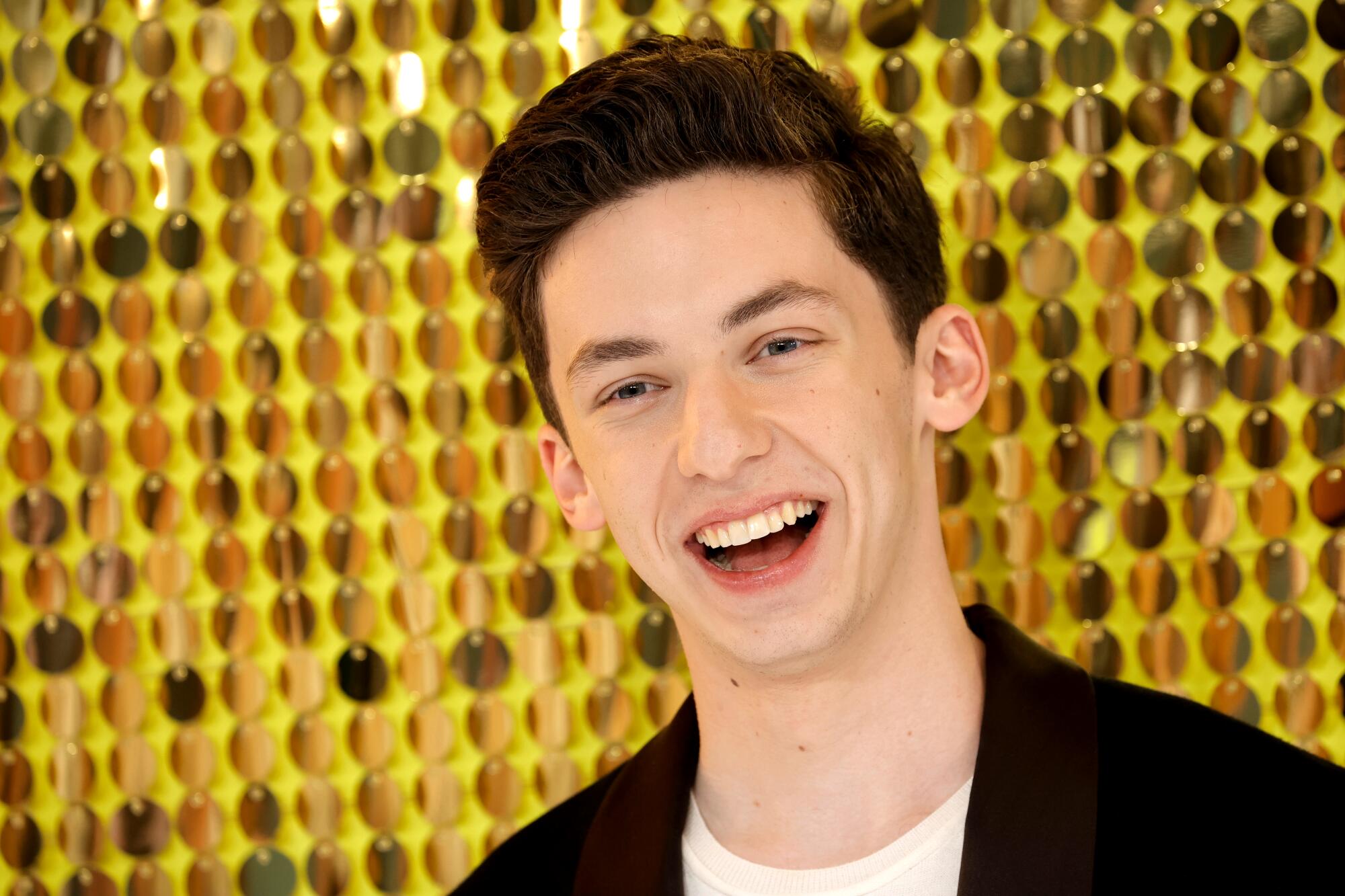 A young man smiles in front of a golden backdrop.