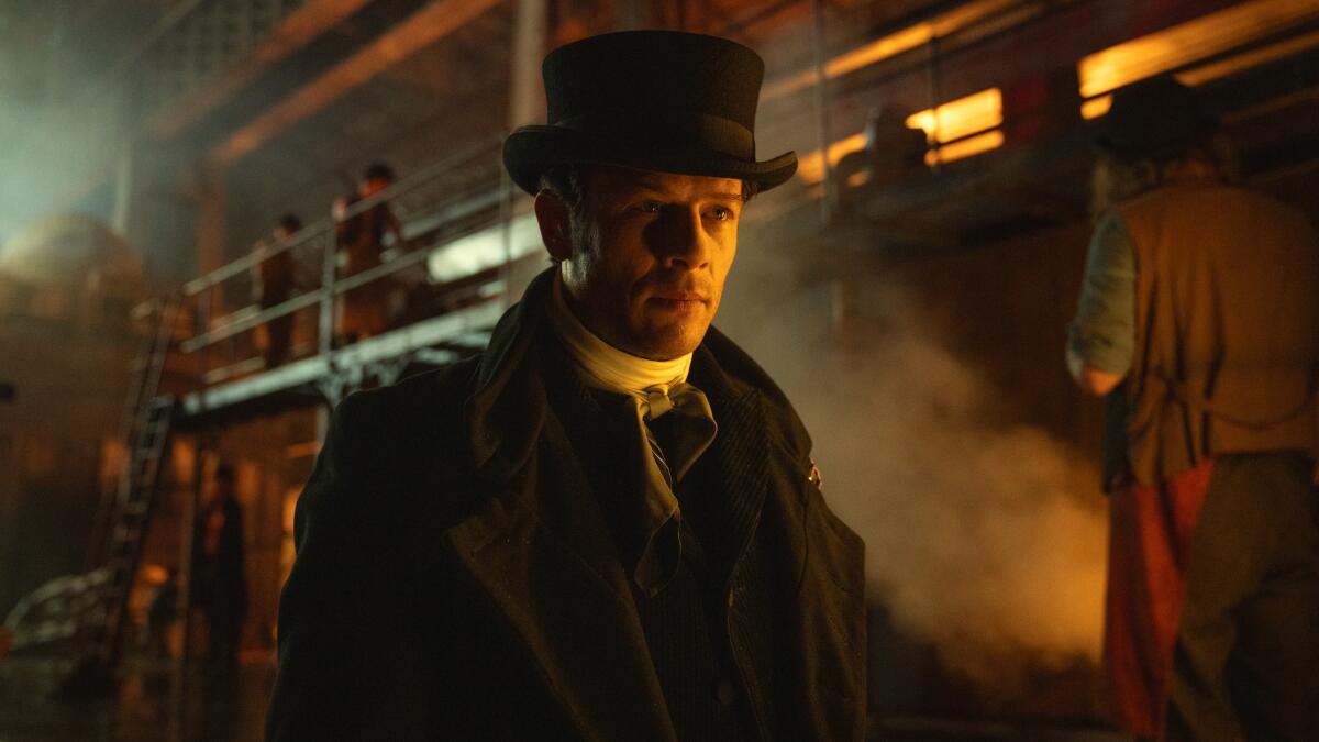 A man in a black top hat walks through a busy warehouse as steam billows around him.