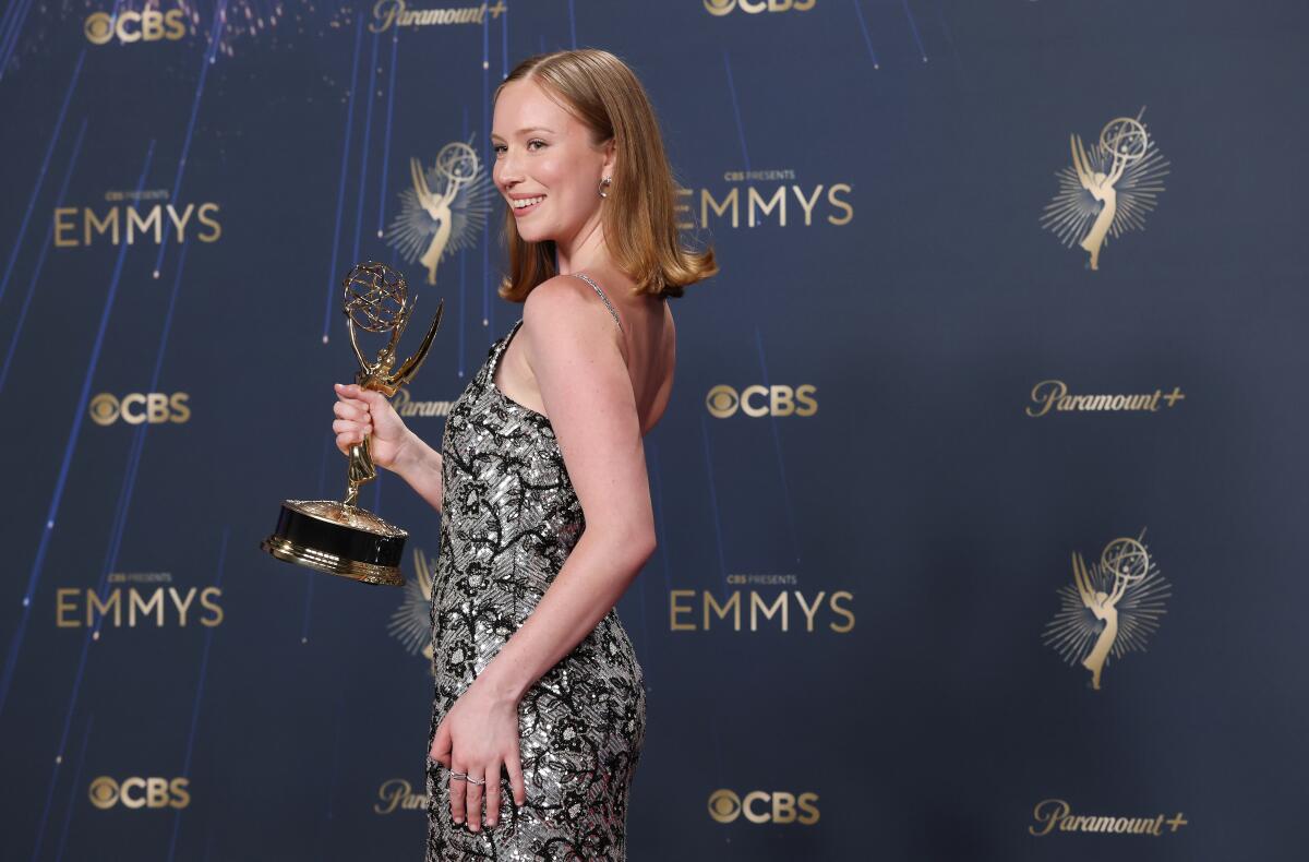 A woman in a black and silver sequined dress seen from the side holding a statuette.