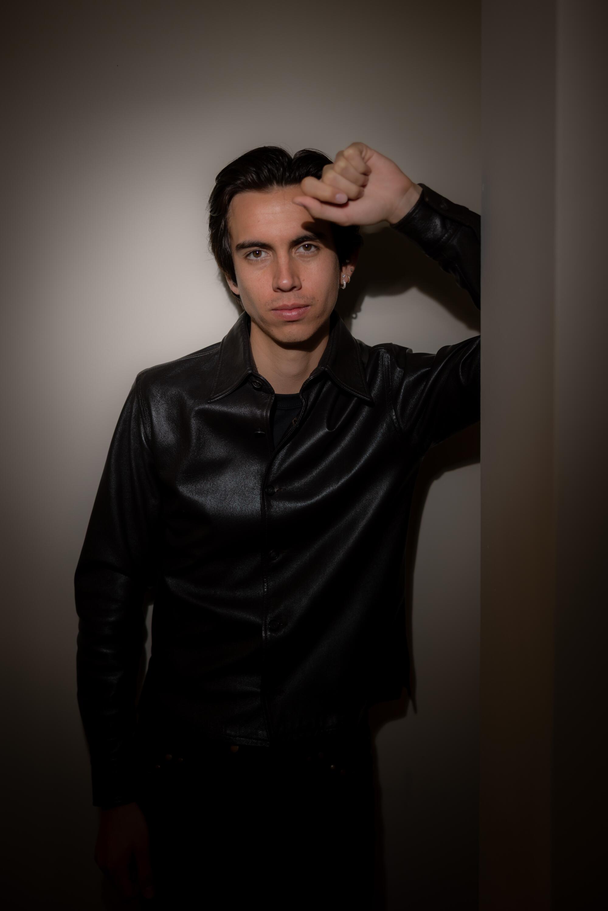 A young man leans against a wall.