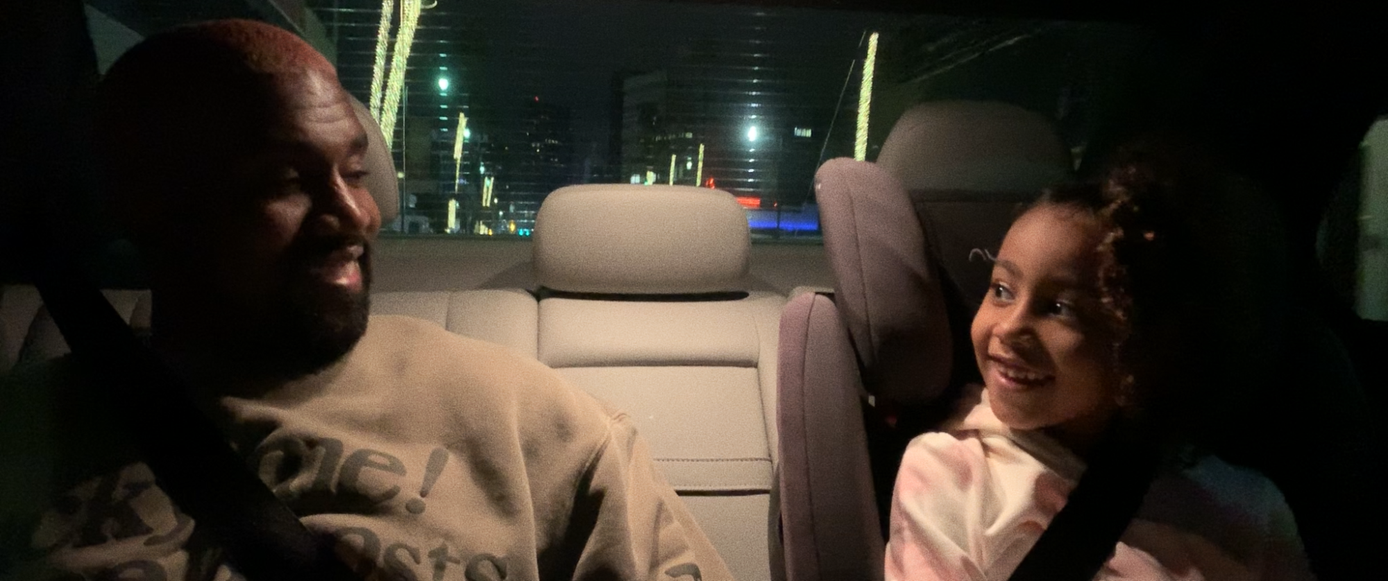 A man and his daughter smile in the back of a car.