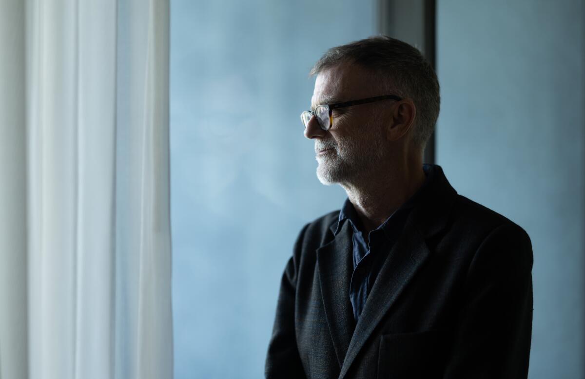 A man with glasses peers out a window
