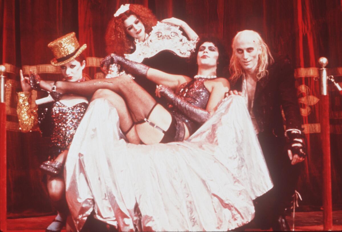 A man in drag sings a song surrounded by performers in a musical.