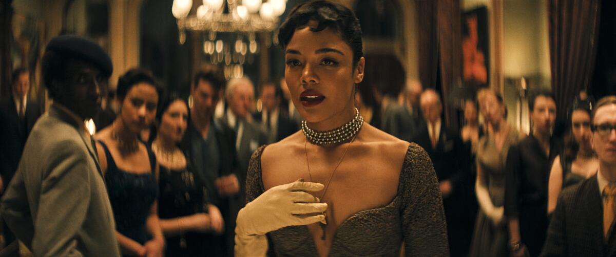 A woman wearing a pearl necklace speaks at a party.