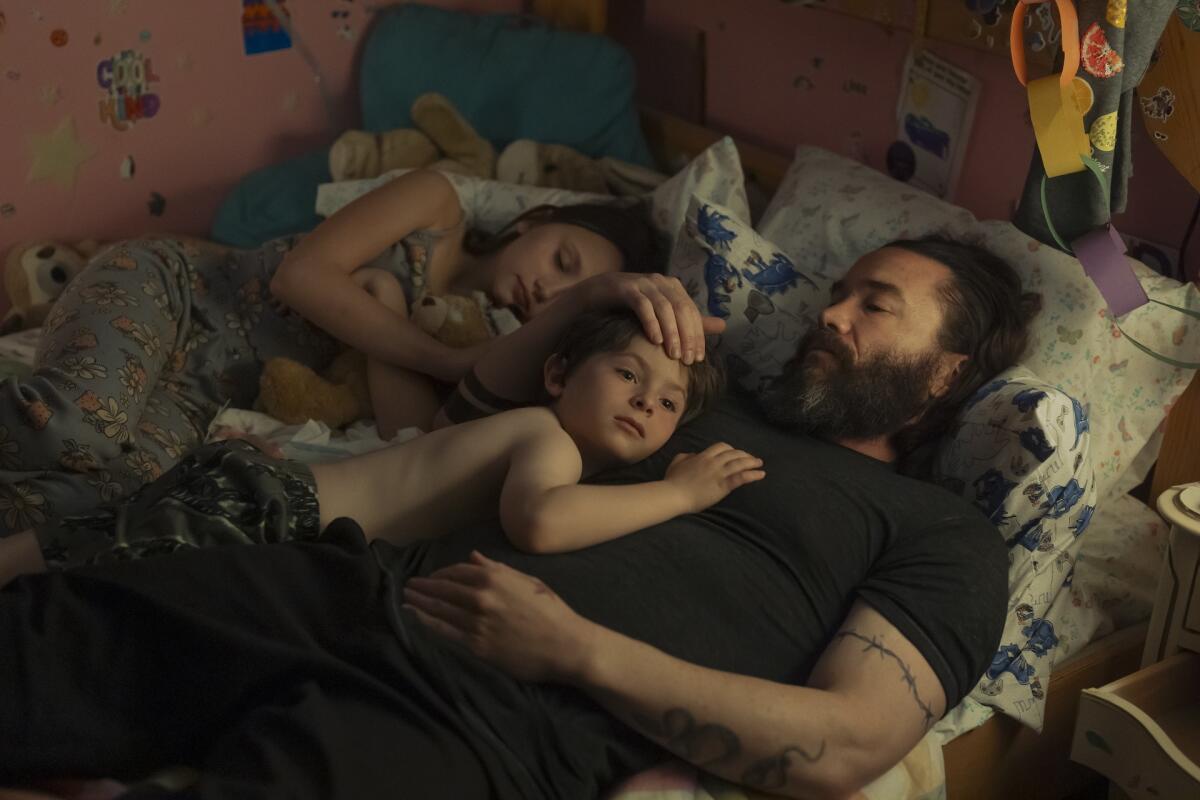 Two children lay in bed with their father.