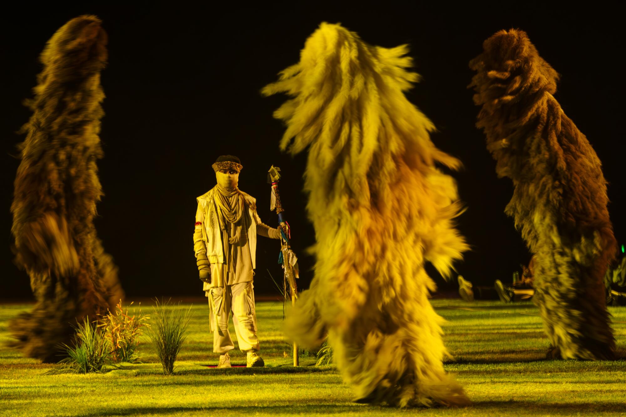 Furry creatures dance on a field in front of an actor. 