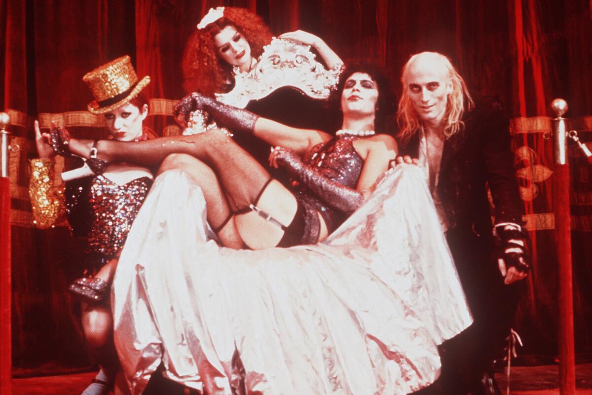 A man in drag sings a song surrounded by performers in a musical.