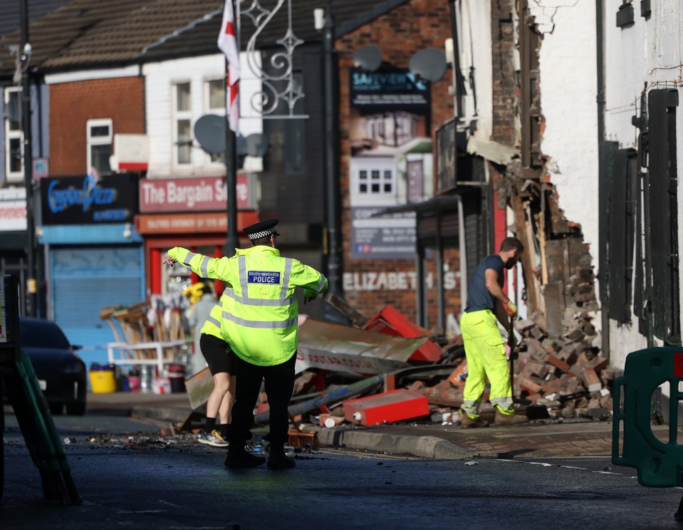 A police officer directs traffic at the scene of a car crash into a building.