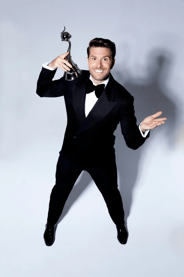Man in tuxedo holding award.