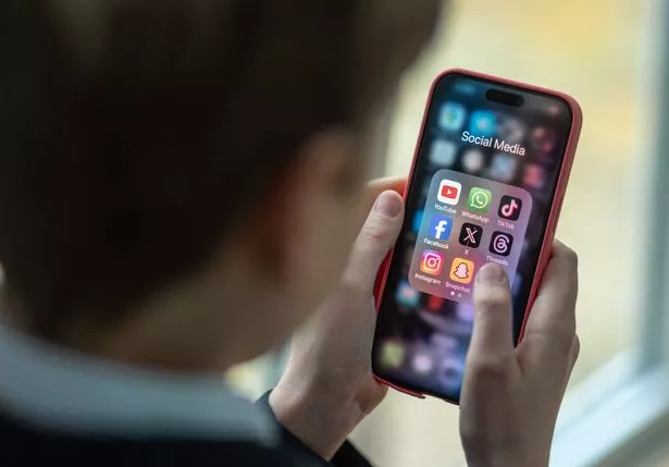 boy looks at an iPhone screen showing various social media apps