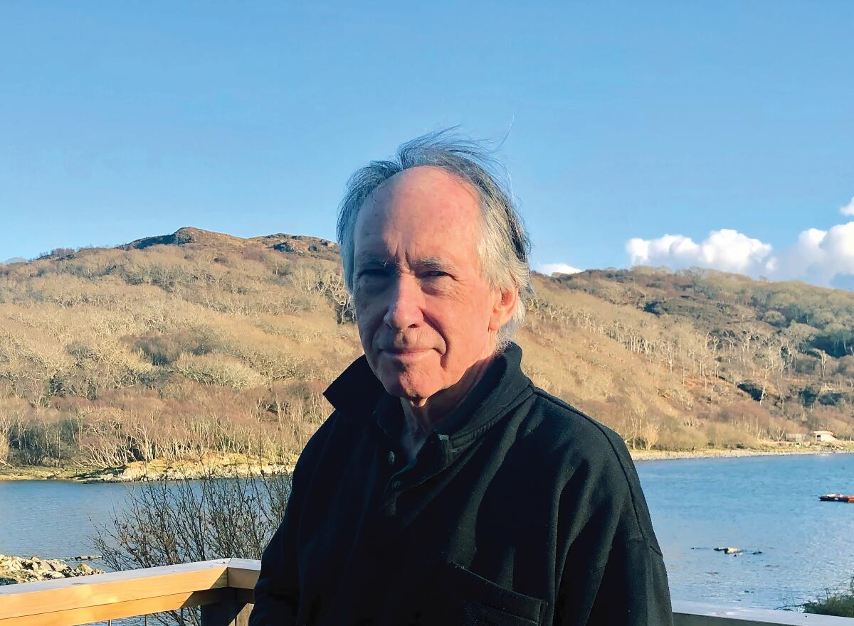 Ian McEwan, wearing a black sweater, stands in front of a lake.