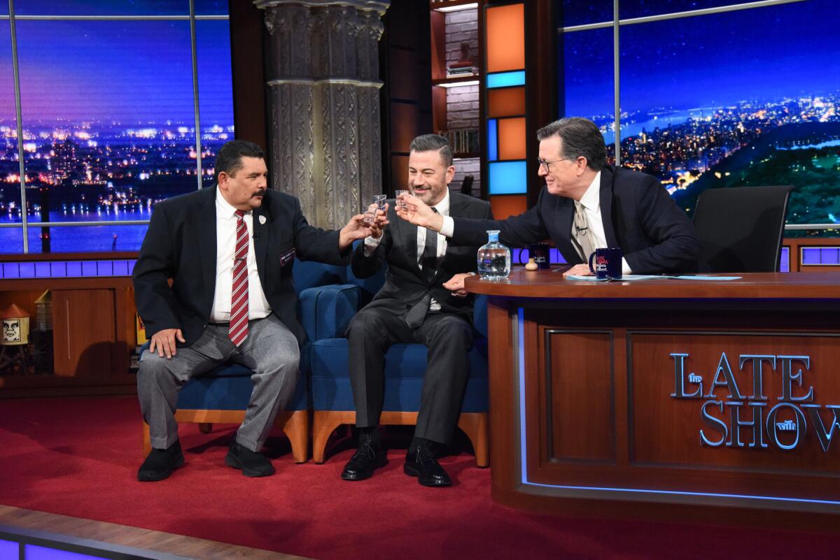 Three men in suits sitting holding shot glasses close together.