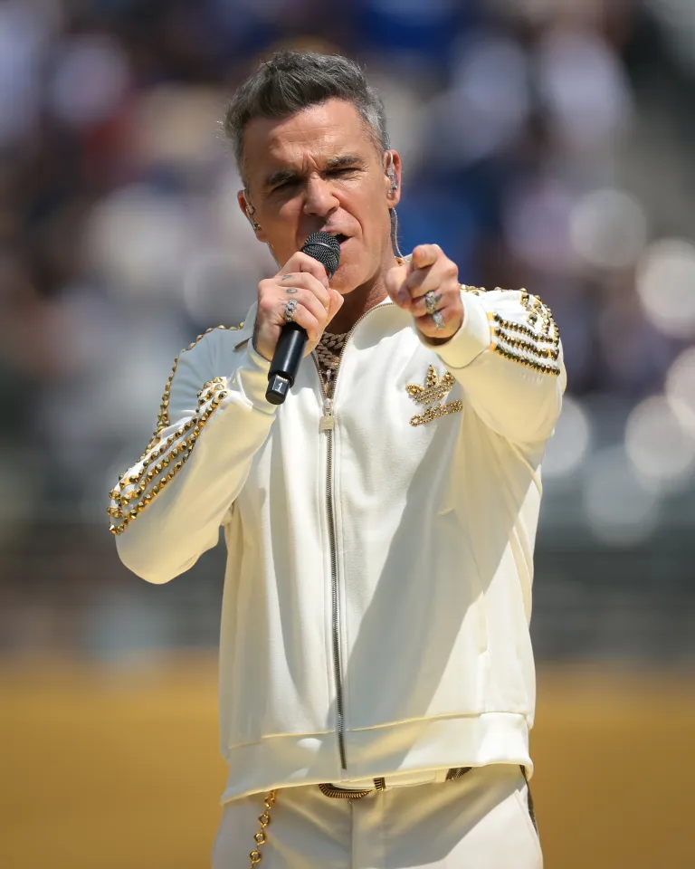 Robbie Williams singing while pointing at the audience.