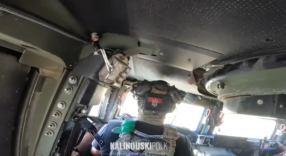 A soldier with a Ukrainian flag patch on their helmet sits inside a military vehicle.