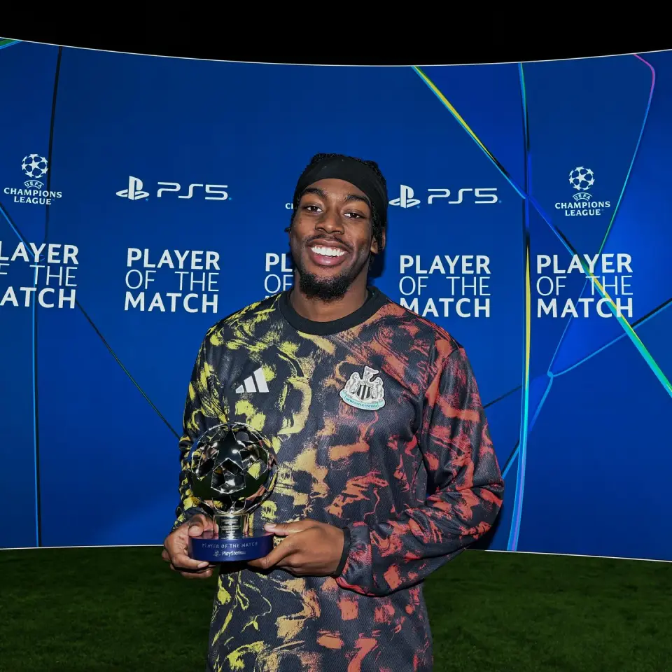 A smiling soccer player holding a "Player of the Match" trophy in front of a blue background with Champions League and Playstation logos.