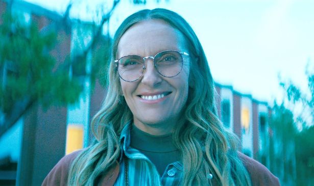 A woman with blonde hair and glasses smiles