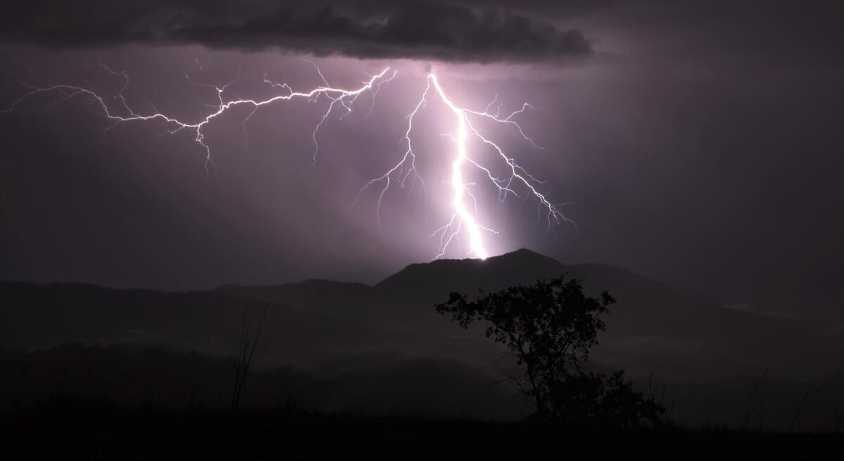 A shock of lightning fractures across the dark sky above a mountain.