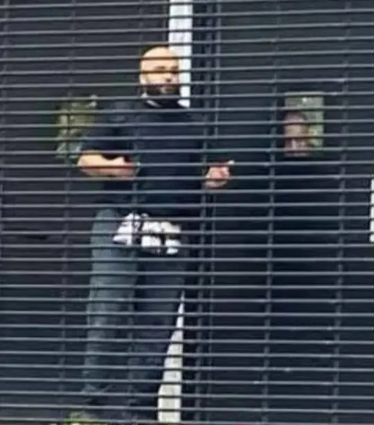 A man looking out from behind a metal gate.