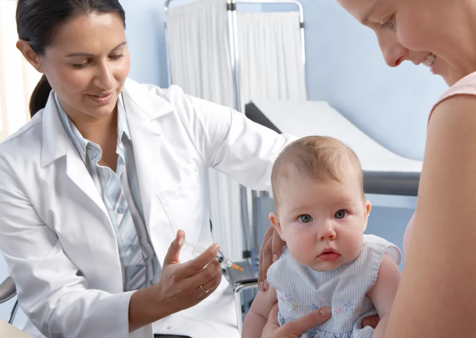 A doctor preparing to give a vaccination to a 5-month-old baby held by an adult.