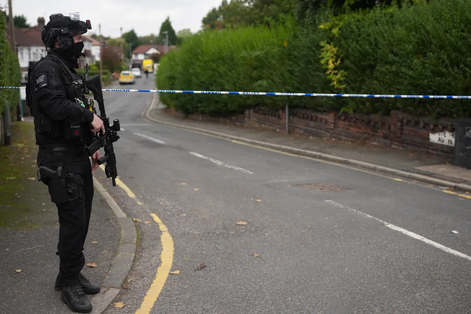 Armed police officer securing the perimeter of a crime scene on White House Avenue in Manchester, England.