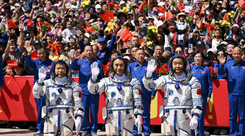 Chinese astronauts Chen Dong, Chen Zhongrui, and Wang Jie wave to a cheering crowd at a send-off ceremony.